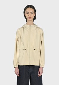 Giacca leggera beige con zip frontale, vita con coulisse e cappuccio. Presenta polsini elasticizzati e un tessuto liscio e textures.