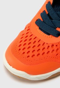 Orange athletic shoe featuring a mesh upper with ventilation holes, navy laces, and a white rubber sole with textured accents.