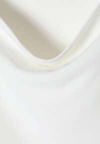 La tela blanca cae suavemente con una textura suave y un ligero brillo. El escote presenta un corte curvado y delicado con bordes limpios.