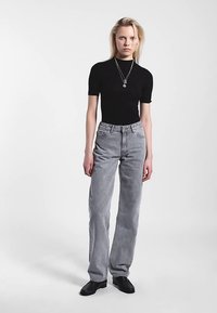 Top nero a maniche corte abbinato a jeans grigi a vita alta e gamba dritta. Tessuto strutturato e design minimalista. Semplice collana d'argento come dettaglio.