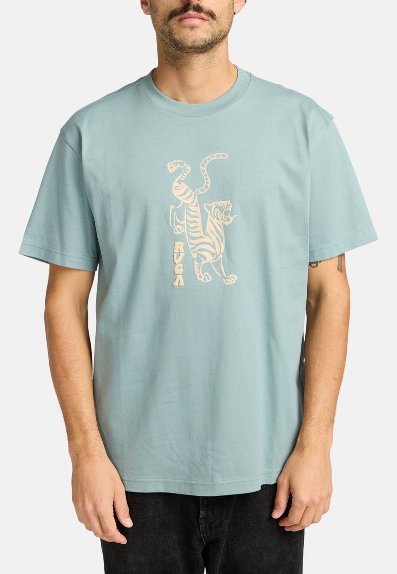  Lichtblauwe katoenen T-shirt met een ronde hals, voorzien van een tan kleurige grafiek van een tijger en de tekst "RUCÁ" eronder. Korte mouwen, ontspannen pasvorm.