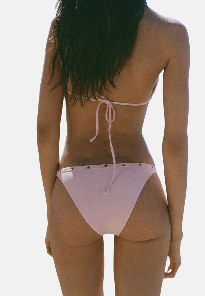 Roza bikini s minimalnim pokrivačem, trakom za vezivanje na leđima i metalnim detaljima duž struka. Glatka tekstura i podesiv kroj.