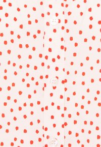 Chemise à boutonnage sur le devant en tissu rose clair avec des motifs de petits points rouges dispersés. Comprend des boutons blancs le long du centre.