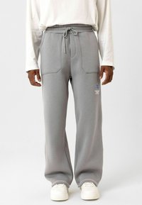 Grijze joggingsbroek met een trekkoord in de taille, zijzakken en geborduurde logo-details. Gepaard met witte sneakers en een langemouwen top.
