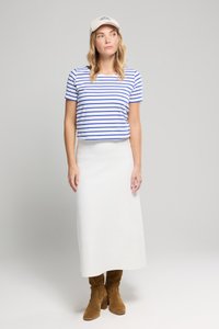 Pasiaka koszulka w niebiesko-białe paski, biała spódnica midi i tanie botki do kolan. Czapka z logo dodaje charakteru stylizacji.