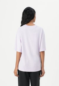 Tricou oversized lavandă cu mâneci scurte, guler rotund, material moale și o croială lejeră; expus din spate pe un fundal simplu.