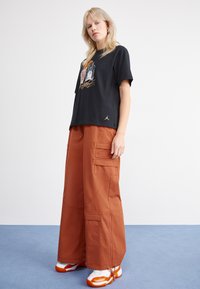 Black cotton T-shirt with graphic print and gold accents, paired with wide-legged, orange cargo pants featuring side pockets and zipper details.