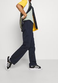 Marina blå byxor med avslappnad passform, bärs med en flerfärgad topp; svarta sneakers med vita ränder fulländar outfiten.