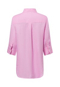 Light pink linen shirt with a collar, long sleeves rolled up, and a back yoke seam. Smooth texture, curved hem, and button cuffs.