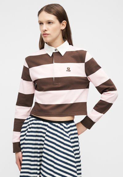Γυναίκα που φοράει ριγέ cropped μακρυμάνικη μπλούζα πόλο σε καφέ και ροζ αποχρώσεις, συνδυασμένη με πλισέ φούστα με ριγέ σε ασπρόμαυρο.
