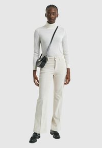 Un pull à col roulé blanc, un pantalon en velours côtelé crème évasé, un sac à bandoulière noir et des mocassins noirs, présentés sur un fond neutre.