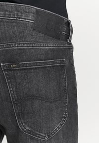 Bolso traseiro e cós de jeans de denim preto da Lee, com a etiqueta de marca em couro e a etiqueta de marca em tecido visíveis.