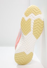 Suela de zapatilla deportiva rosa con patrones texturizados; presenta una sección blanca en forma de onda y una suela de goma amarilla con pequeños puntos y surcos.