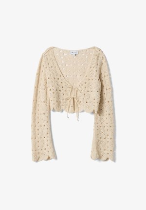 Beige gehaakt gebreid cropped vest met lange mouwen, getande randen en een striksluiting aan de voorkant.