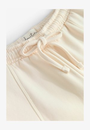 Hellbeige Baumwollshorts mit einem elastischen Bund, ausgestattet mit einem Kordelzug und einem Etikett mit kursivem Text. Glatte Textur und schlichtes Design.