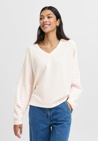 Lichtroze V-hals pullover met witte strepen, gemaakt van een textuurstof. Losse pasvorm met lange mouwen en een gebogen zoom. Gecombineerd met blauwe denim.