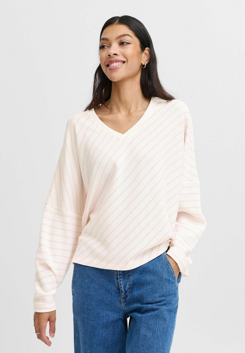 Lichtroze V-hals pullover met witte strepen, gemaakt van een textuurstof. Losse pasvorm met lange mouwen en een gebogen zoom. Gecombineerd met blauwe denim.