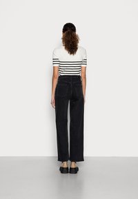 Krótka bluzka w czarno-białe paski z krótkim rękawem, zestawiona z wysokim stanem czarnych szerokich spodni dżinsowych. Gładka faktura, casualowy design z wyraźnym przeszyciem.