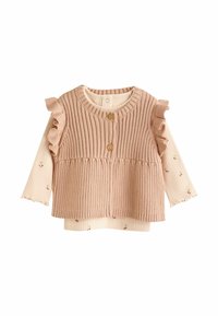 Chaleco de punto rosa acanalado con hombros con volantes y botones de madera, superpuesto a una camiseta de manga larga color crema con pequeños patrones florales.