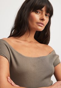 Haut khaki à épaules dénudées en côtes, avec des manches courtes, présentant un design ajusté et une texture lisse. Un subtil éclat rehausse l'apparence générale.