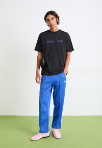 Sort bomulds T-shirt med blå og rød grafisk print, parret med blå træningsbukser og lyserøde sko. Læder crossbody taske over skulderen.