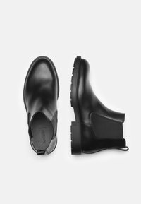 Bottes Chelsea en cuir noir avec des panneaux élastiques sur les côtés, bout rond et semelle en caoutchouc texturé, dotées d'une languette pour un enfilage facile.