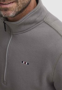 Pullover grigio a zip corta realizzato in tessuto morbido, con un piccolo logo ricamato con righe rosse, bianche e blu sul petto.