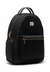 Sac à dos Herschel noir avec fermetures éclair dorées, poches avant et latérales, et doubles poignées supérieures, positionné légèrement incliné à droite sur un fond blanc.