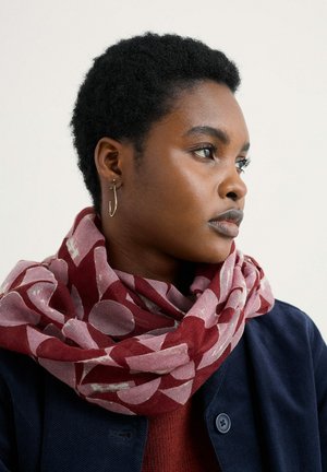 Red and pink patterned scarf wrapped around the neck, made of lightweight fabric, featuring circular shapes and a soft texture.