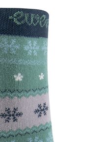 Chaussettes tricotées avec un motif en vert, bleu et beige, comportant des flocons de neige et des rayures ondulées. Fini avec une bordure en vert foncé.