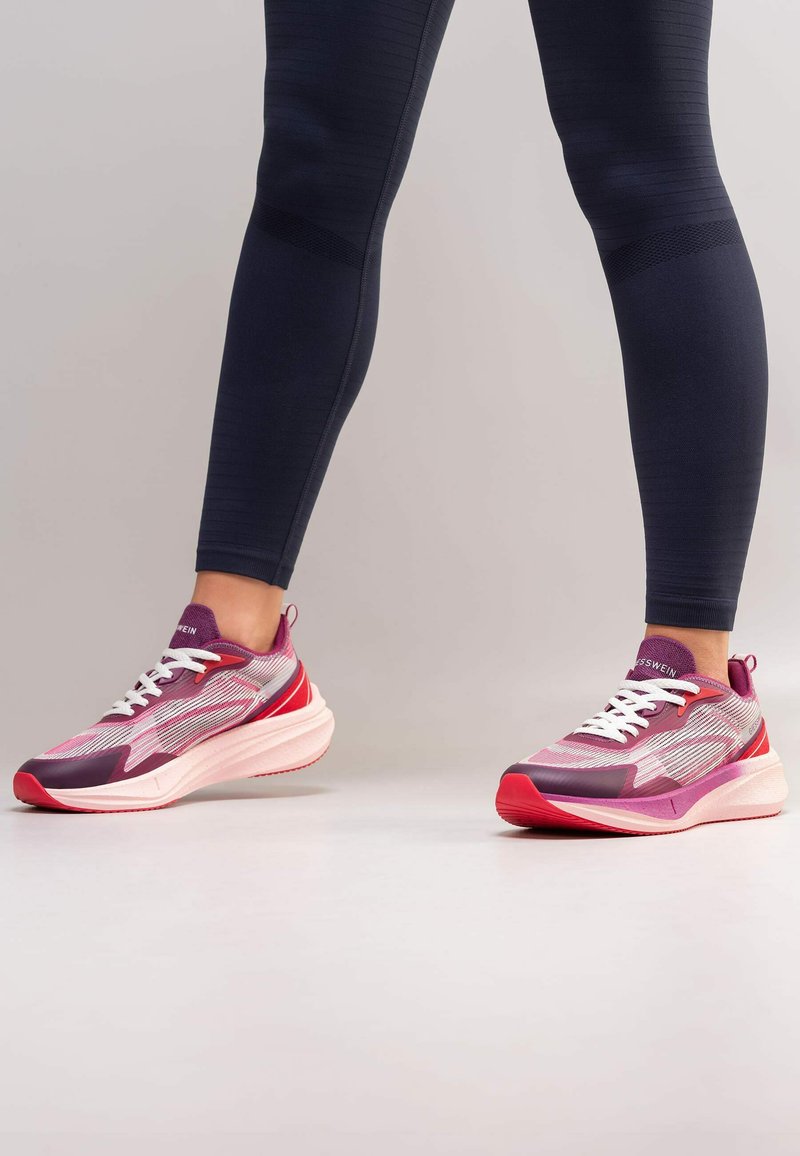 Chaussures de sport violettes et roses avec un design en maille et des lacets blancs. Elles possèdent une épaisse semelle blanche et des accents texturés sur les côtés.