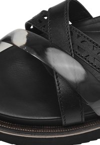Sandale en cuir noir avec des sangles croisées, accent noir brillant, surface texturée et semelle intérieure ergonomique pour le confort.