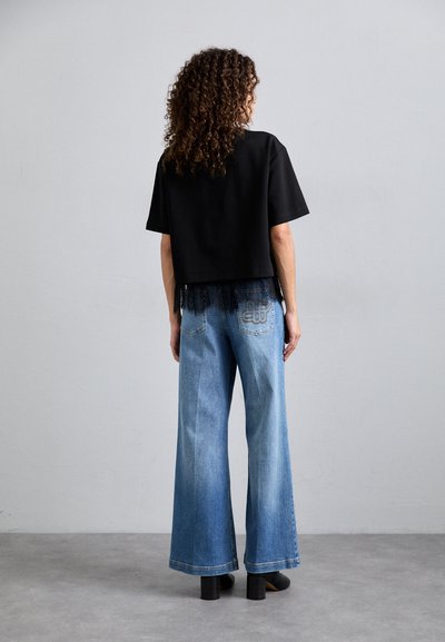 Czarna wycięta koszulka z koronkowym detalem na końcu, w połączeniu z jasnoniebieskimi szerokimi dżinsami. Modelka ma na sobie czarne buty na słupku.