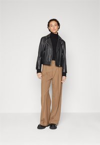 Schwarze Lederbikerjacke über einem schwarzen Rollkragenpullover, kombiniert mit hoch taillierten, weiten braunen Hosen und klobigen schwarzen Stiefeln.