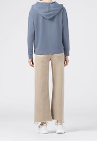 Hoodie i mjuk blå bomull, kombinerad med ljusbeige byxor med vida ben och fransiga fållar. Vita sneakers fullbordar outfiten.