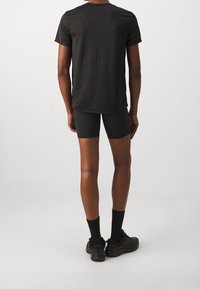 Camiseta negra de manga corta, pantalones cortos negros ajustados, calcetines negros y zapatillas deportivas. Tejido suave, diseño sencillo y colores neutros.