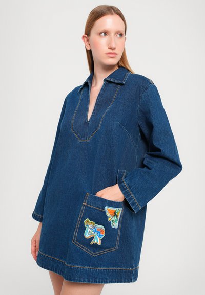 Denim dress with a collared neckline, long sleeves, and a front pocket featuring colorful patches. Stitching is contrasting yellow.