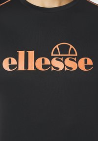 Black shirt with large orange "ellesse" logo and half-circle graphic centered on the chest, worn by a person.
