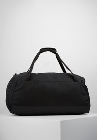 Borsone nero realizzato in tessuto resistente, di forma cilindrica, dotato di due manici superiori, chiusura a zip e una tasca laterale in rete.