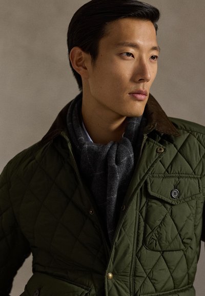 Zaļa kapučveida jaciņa ar korduroja apkakli, pelēku šalli un pogātu krūšu kabatu. Gluda tekstūra, silts dizains un praktiskas detaļas.