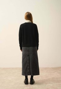 Svart stickad tröja, vit polo-krage, grå denimkjol med en bakre slits, svarta ankelboots, slät textur, avslappnad passform.