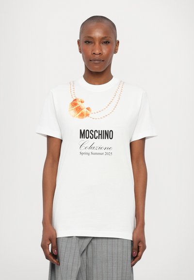 Biała bawełniana koszulka z grafiką croissanta i naszyjnika z pereł. Napis brzmi "Moschino Colazione Wiosna Lato 2025". Krótkie rękawy.