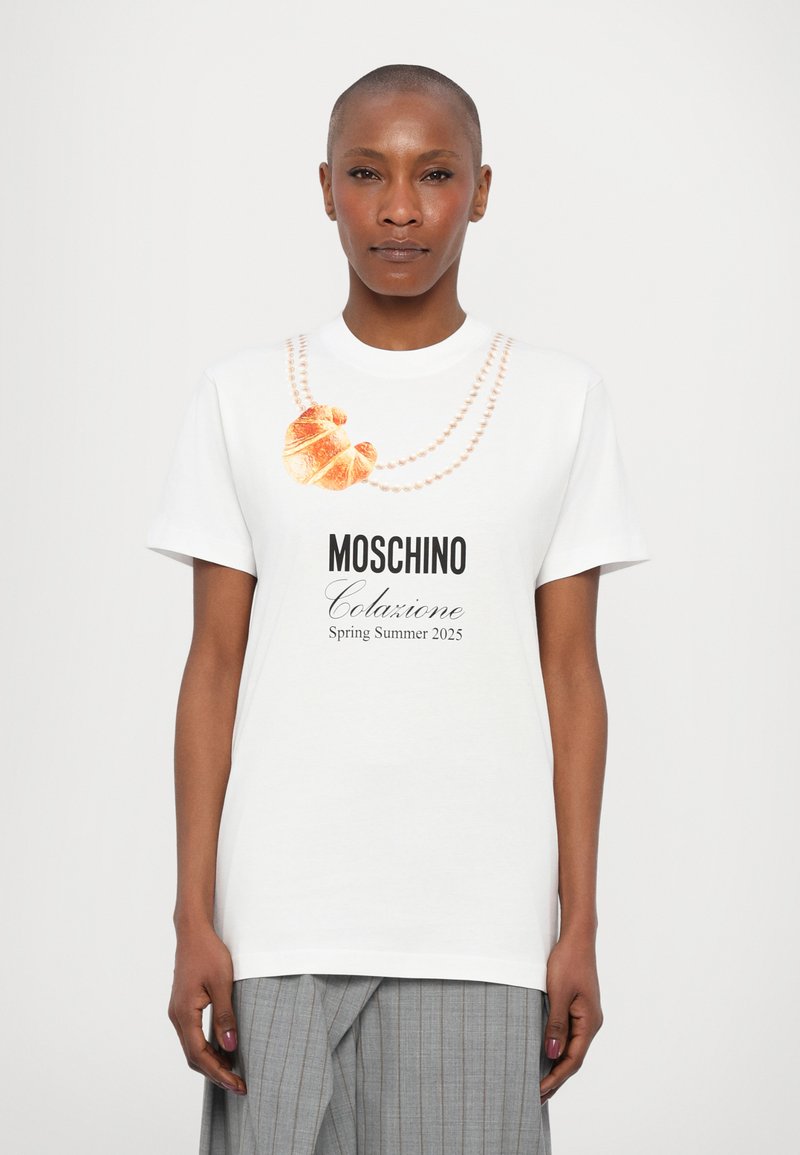 Balta kokvilnas T-krekls ar kruasāna grafiku un pērļu virtenēm. Uzraksts "Moschino Colazione Pavasaris Vasaras 2025." Īsas piedurknes.