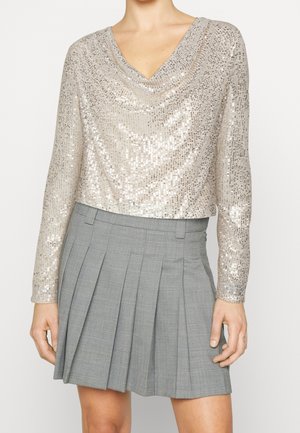 Korte, lange mouw top in metallic beige pailletten, met V-hals ontwerp. Gecombineerd met een grijs geruit plissérok. Vlakke textuur, glanzende afwerking.