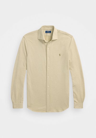 Beige hosszú ujjú poloing, texturált anyagból. Klasszikus gallérral, gombos záródással és egy kis logóval a mellkason.