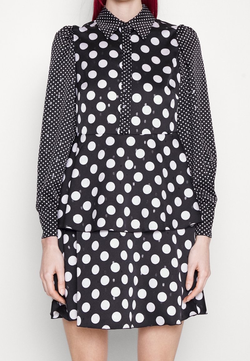 Robe noire à manches longues avec de grands pois blancs sur le corps et de petits pois blancs sur les manches et le col.