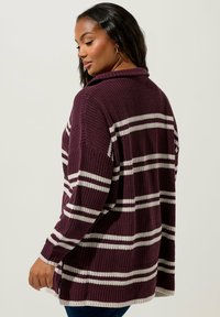 Mörkröd stickad cardigan med vita horisontella ränder, lös passform, ribbad textur och sjalkrage. Sidofickor förbättrar rörligheten.