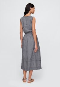 Svartvit ginghamklänning med korta volangärmar, elastisk midja och en kjol i midjelängd. Har en enkel baksidesdesign och casual sandaler.