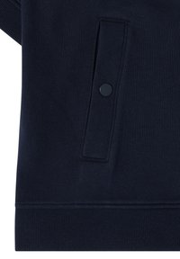 Tissu de vêtement bleu marine foncé avec une poche fendue verticale sécurisée par un seul bouton-pression noir et un ourlet côtelé en bas.