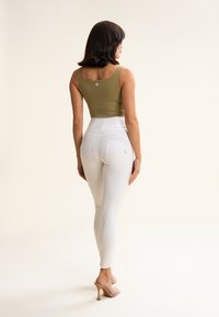 Top ajustado de tirantes en verde oliva con una etiqueta de logo; leggings blancos de tiro alto con paneles texturizados y detalles de costura en la parte trasera.